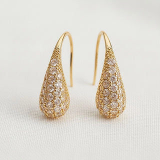 Gold pavé cubic zirconia teardrop dangle earrings - angled view on white linen background