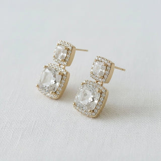 Double cushion-cut CZ halo drop earrings gold tone - angled side view on white linen