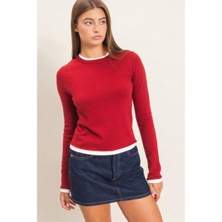 Fitted red long sleeve knit top with white contrast trim at the crew neckline, cuffs, and hem, styled with a denim skirt