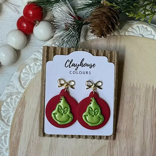 Close-up of handmade red and green Grinch-inspired polymer clay holiday earrings with bow accents