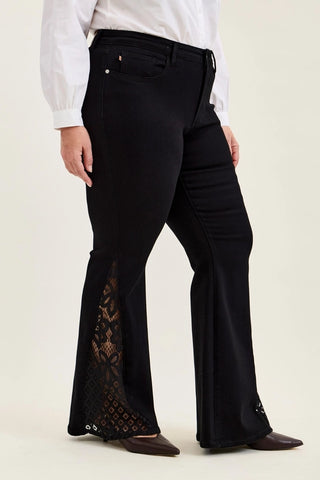 Model wearing plus size black Judy Blue Jaqueline ultra flare jeans with lace inserts at the hem.