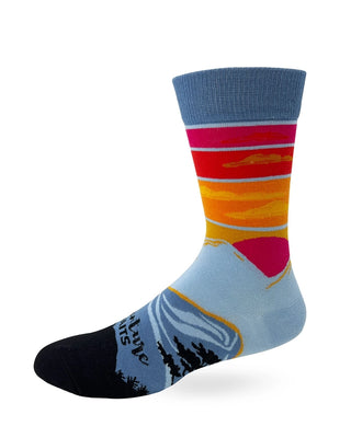 Opposite side of Adventure Awaits crew sock showing warm sunset colors, a red sun, blue mountain imagery, and black tree silhouettes